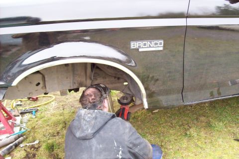 1995 Ford Bronco - A person works on the fender of a dark green 1995 Ford Bronco, with the vehicle's side badge clearly visible.