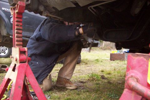 1995 Ford Bronco - A person works on the underside of a vehicle supported by jack stands, with another Bronco in the background.