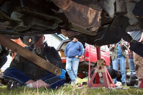 1995 Ford Bronco - Multiple individuals are gathered around the undercarriage of a red SUV, appearing to perform maintenance.