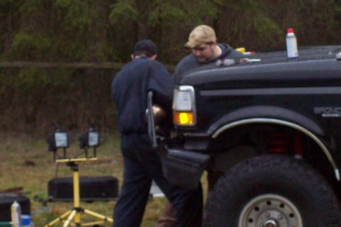 1995 Ford Bronco - A black 1995 Ford Bronco is shown with two individuals working on it, and red suspension components are visible.