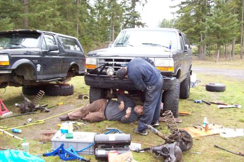 1995 Ford Bronco - Mechanics perform repairs on two Ford Broncos outdoors, with one vehicle elevated for service.