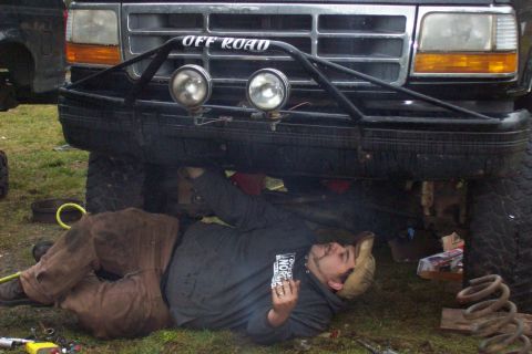 1995 Ford Bronco - A person works on the underside of a lifted truck, with the front grille and bumper visible.