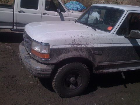 1979 Ford Bronco - A muddy white Ford F-Series pickup truck is parked off-road in the dirt. The front passenger side of the truck is visible, showing its head…