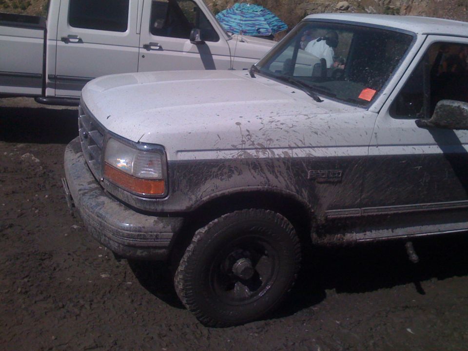 Muddy white Ford F-Series pickup truck, front passenger side view.
