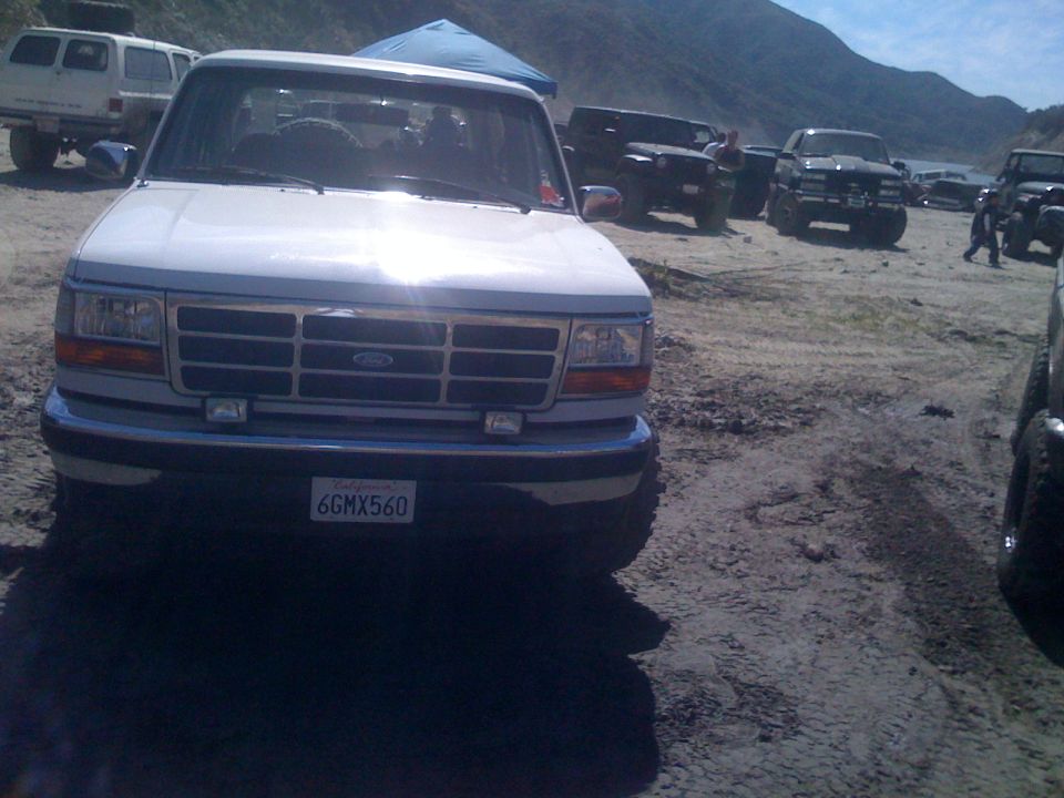 White Ford pickup truck with license plate 6GMX560 parked in a dirt lot with other vehicles.