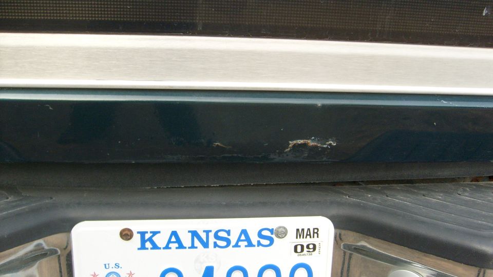 Rear of dark green vehicle with paint chips and Kansas plate, MAR 09 sticker