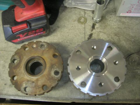 1996 Ford Bronco - A rusty, used differential flange is shown next to a new, shiny replacement flange. A red and black cordless drill is visible in the backgr…