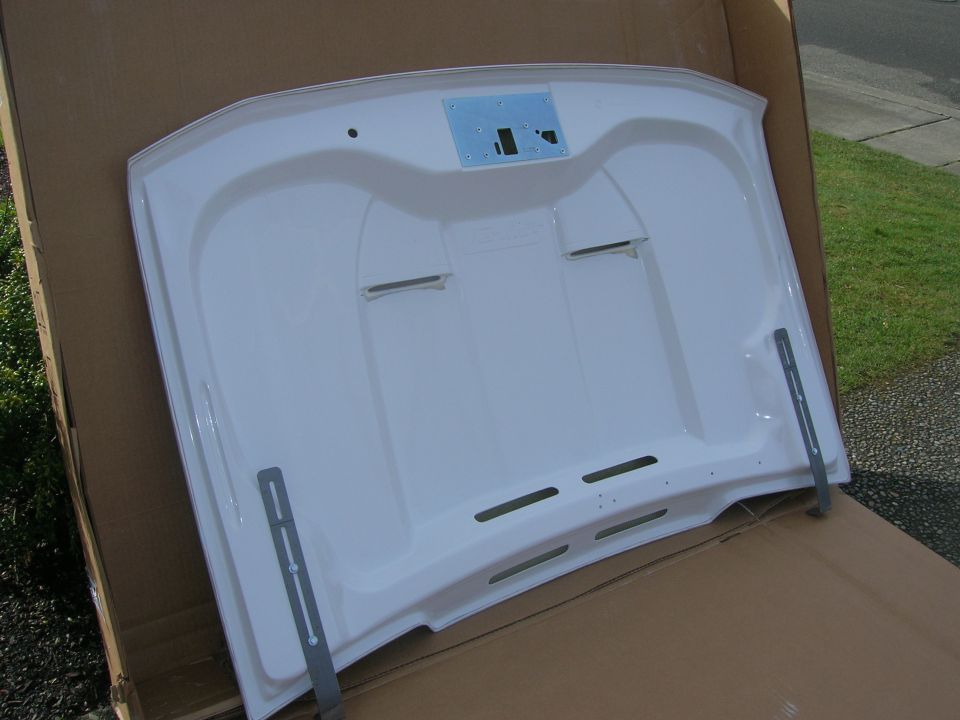 White vehicle hood inside a box, showing underside with mounting brackets.