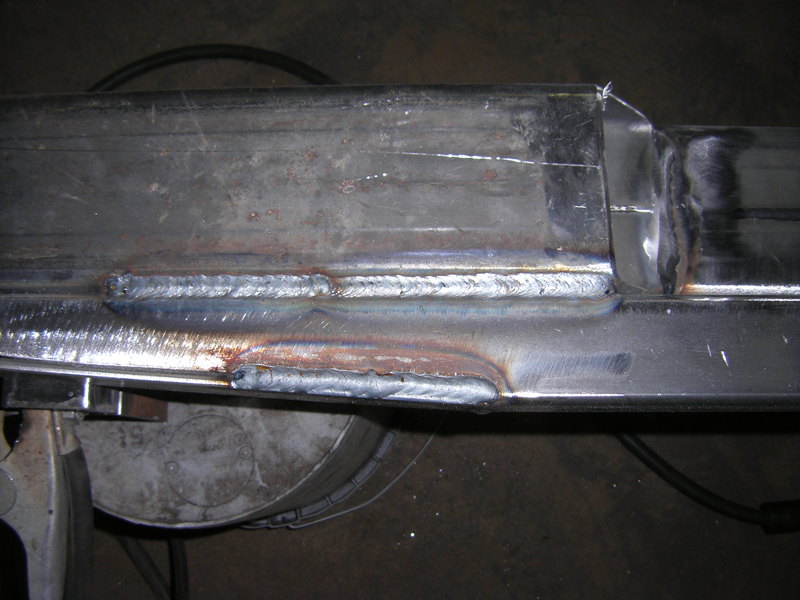 Close-up of fresh weld beads joining bare steel bumper channel to plate on a workbench