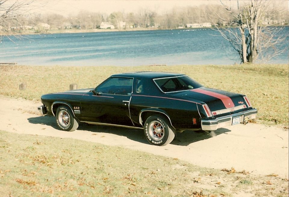 Black 1970s coupe with red racing stripes parked by a lake.