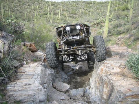 1987 Suzuki Samurai - A heavily modified off-road buggy, likely a Suzuki Samurai, navigates a rocky, desert trail with saguaro cacti in the background.