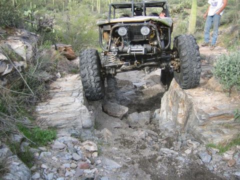 1987 Suzuki Samurai - A modified off-road vehicle navigates a rocky trail, with its front right tire perched on a large rock. The vehicle appears to be a custom…