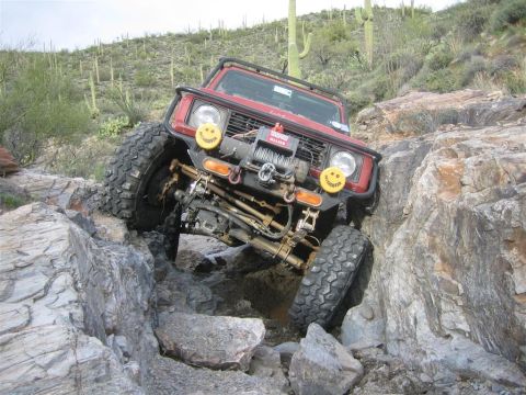 1987 Suzuki Samurai - A red off-road Suzuki Samurai is navigating a rocky, desert terrain with its front tire high on a rock. The vehicle features a winch and au…