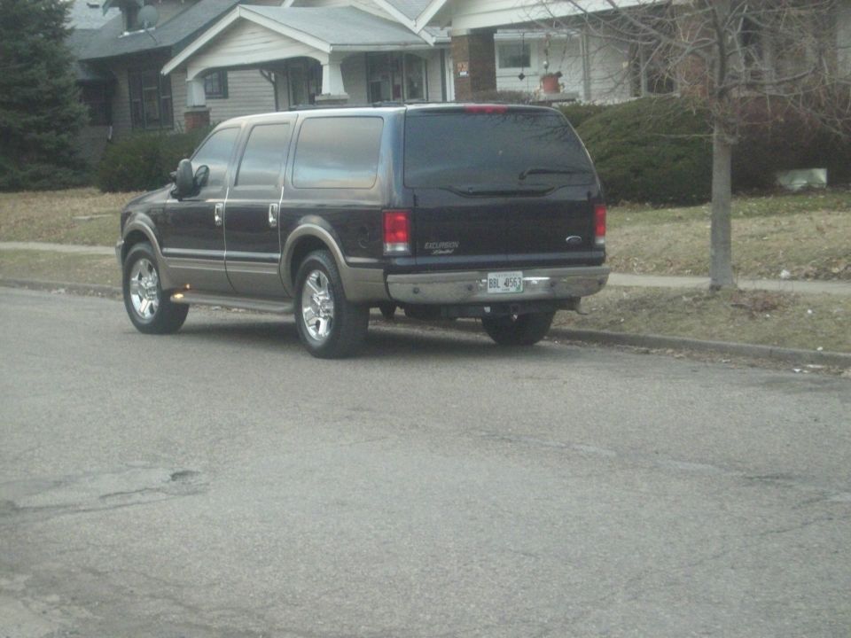 Dark Ford Excursion Limited SUV with tan lower trim parked curbside, rear three-quarter view