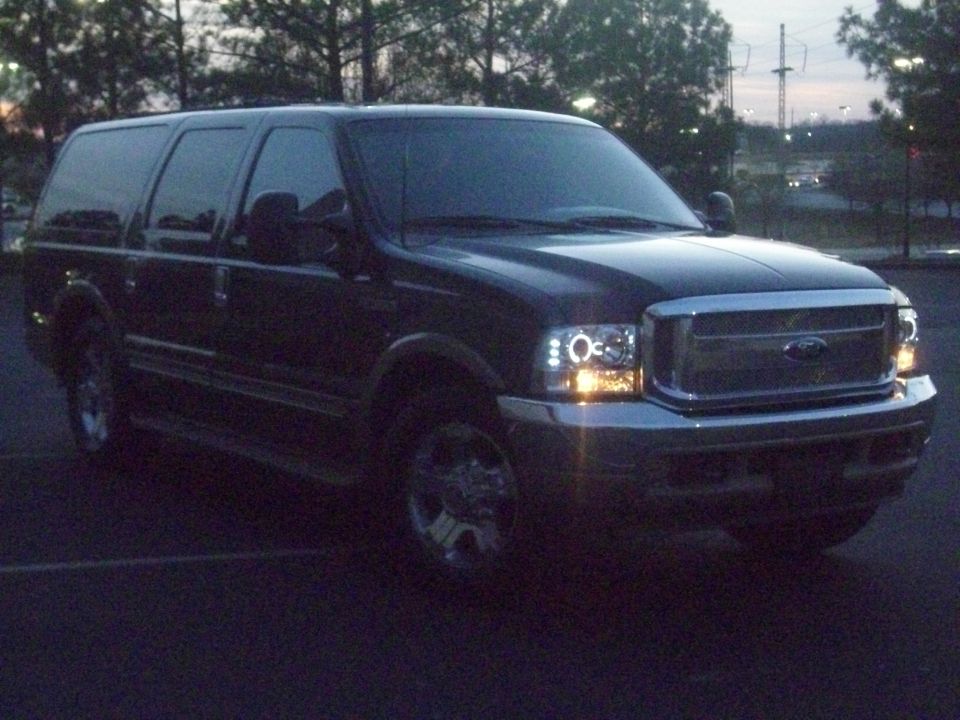 Black Ford Excursion SUV with headlights on in a parking lot at dusk
