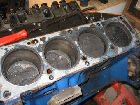 1966 Ford F-100 - A close-up view of a disassembled V8 engine block with four cylinders visible. Pistons are present in each cylinder, covered in carbon buil…