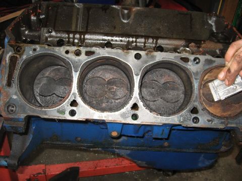 1966 Ford F-100 - Teardown view down onto one bank of a blue-painted V8 engine block with the cylinder head removed, showing four carbon-caked piston tops an…