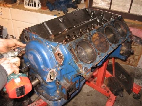 1966 Ford F-100 - A blue V8 engine block is being worked on with a drill and other tools. The engine is mounted on a red engine stand in what appears to be a…