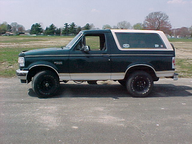 Dark green two-door Ford Bronco with white top, side view, parked on pavement