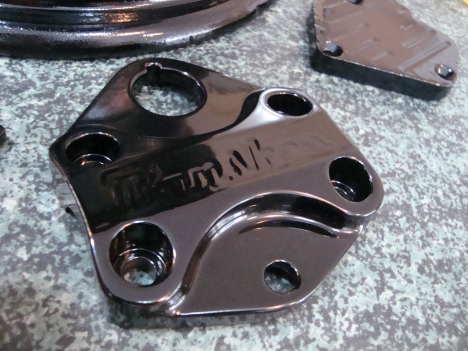 Shiny black metal vehicle part with "T-Rex" text and multiple holes.