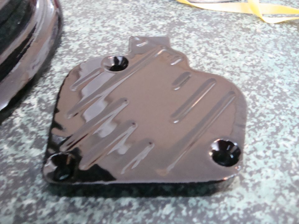 Glossy black automotive part with embossed lines and screw holes on a speckled surface.