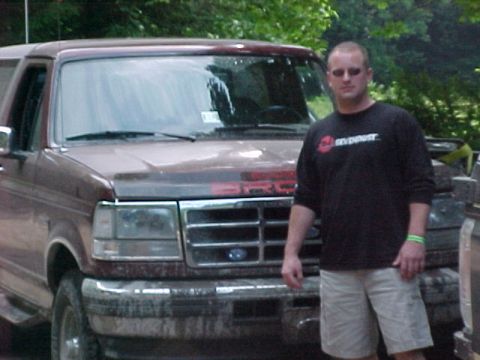 1993 Ford Bronco - A dark red full-size Ford Bronco caked in dried mud sits nose-out under trees, with mud spatter across the hood, grille and headlights and…