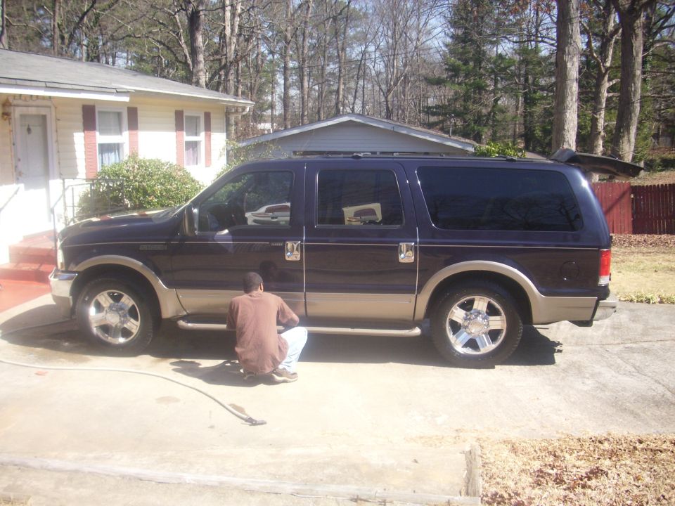 Black and tan Ford Excursion in a driveway with a person crouched at a wheel