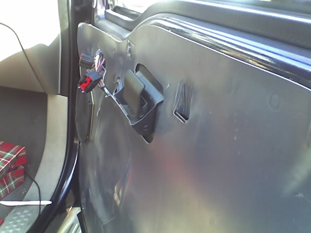 Inside of a vehicle door panel with exposed wiring harness and door handle linkage