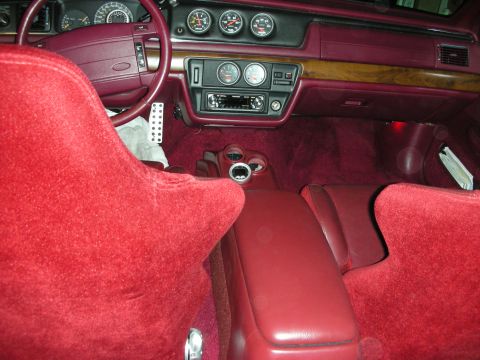 1992 Ford Crown Victoria - The interior of a car with red velour seats and carpeting is shown. The dashboard features a burgundy steering wheel, a radio, and multiple…