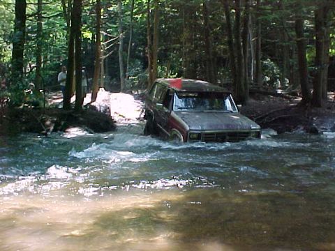 1993 Ford Bronco - A maroon full-size Ford Bronco with an orange whip flag drops off a bank into a fast-moving creek in the woods, water washing up over the f…