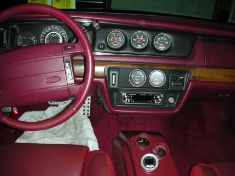 1992 Ford Crown Victoria - The interior of a 1992 Ford Crown Victoria features a burgundy dashboard with multiple gauges, a wood-grain trim accent, and a red steering…