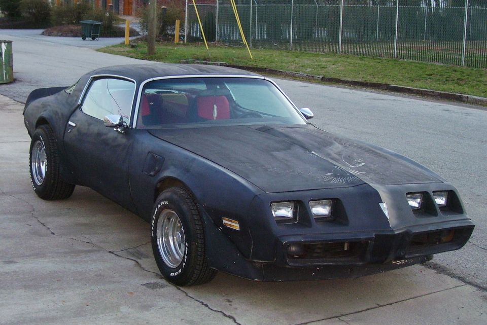 Black 1978 Pontiac Trans Am with red interior and chrome wheels parked on a street.