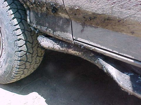 1993 Ford Bronco - Close-up of trail damage along a rocker panel and running board, crushed and bent inward with the paint scraped down to bare metal and mud…