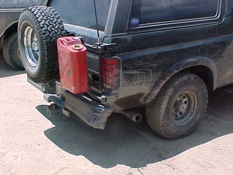 1993 Ford Bronco - Rear corner of a dark full-size Bronco fitted with a heavy tubular rear bumper and tire carrier holding a mud-terrain spare, plus a red ste…