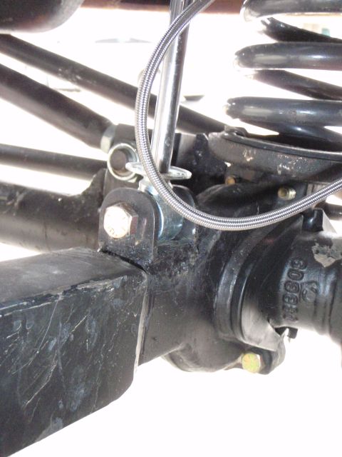 1996 Ford Bronco - A close-up view shows the suspension components of a vehicle, including a black metal arm, a silver coil spring, and a braided metal cable…
