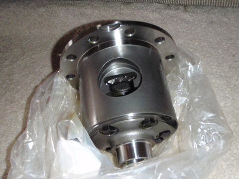 1996 Ford Bronco - A new differential locker is shown, partially wrapped in clear plastic, resting on a carpeted surface. The differential is made of polished…