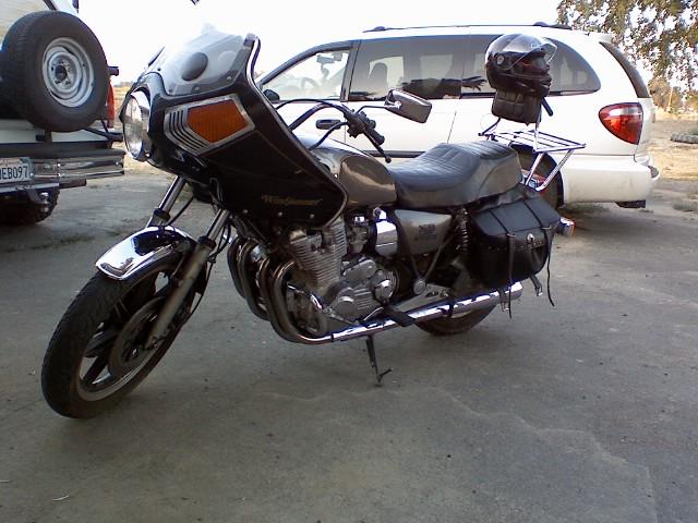 Black motorcycle with front fairing parked on concrete, helmet on rear rack, minivan behind.