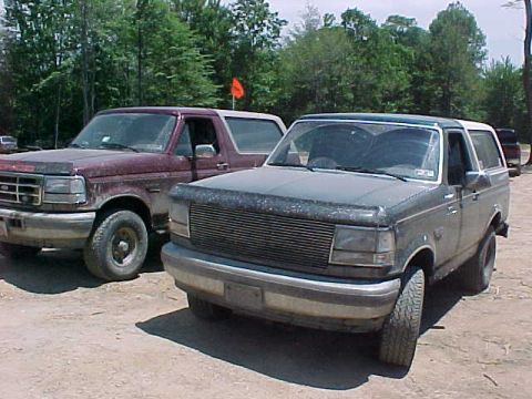 1993 Ford Bronco - Front three-quarter view of a mud-splattered dark green full-size Ford Bronco with a white roof, blacked-out grille and chrome bumper, park…