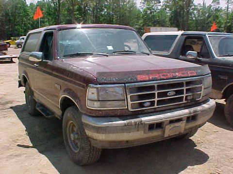 1993 Ford Bronco - Front three-quarter view of a dust-caked maroon full-size Ford Bronco with a red BRONCO hood decal, chrome-trimmed grille and bumper, and a…