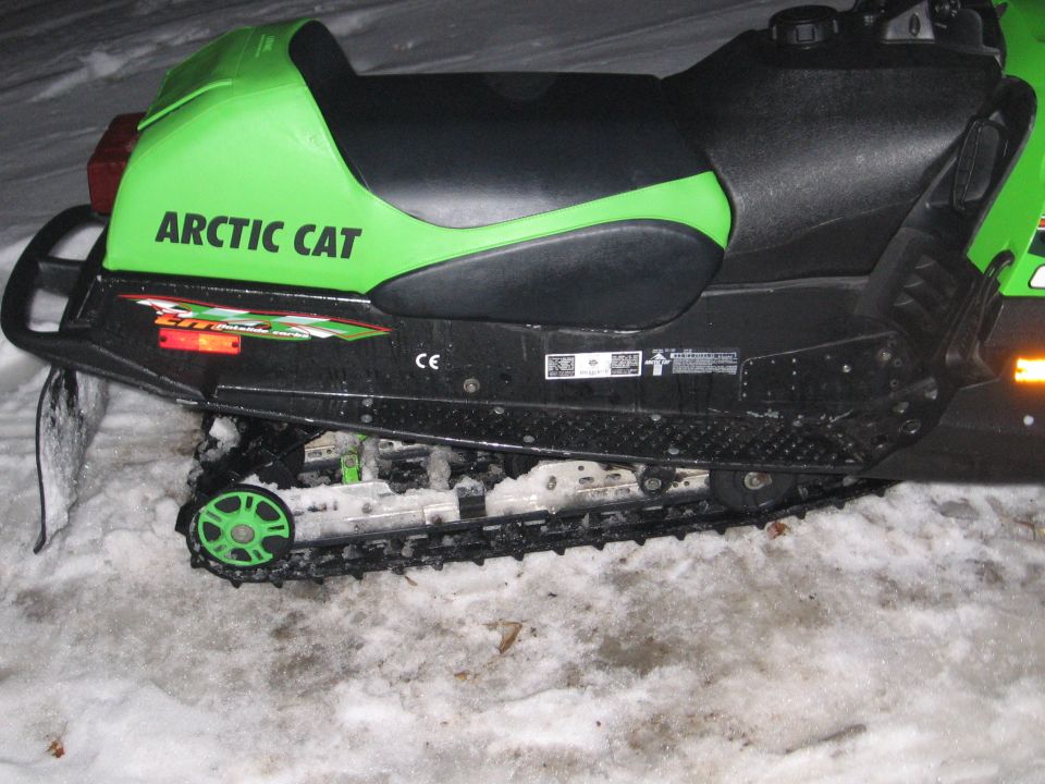 Green and black Arctic Cat snowmobile parked on snow at night