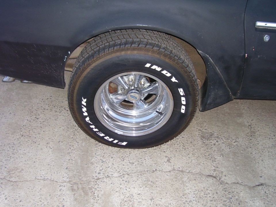 Rear tire and fender of a dark vehicle with Firehawk Indy 500 tires and chrome rims.