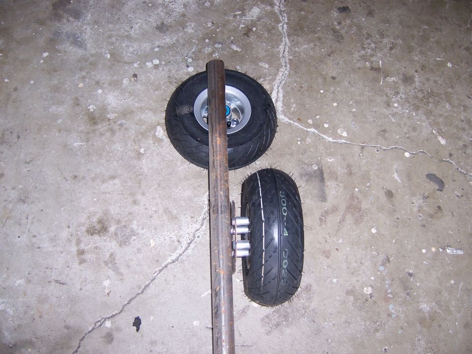 Two small pneumatic wheels mounted on a steel axle on concrete