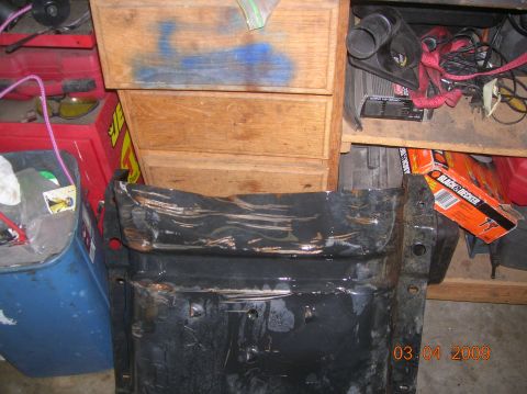 1985 Ford Bronco - A heavily damaged and dented black metal part, possibly a skid plate or bumper component, is shown in the foreground. Behind it are wooden…