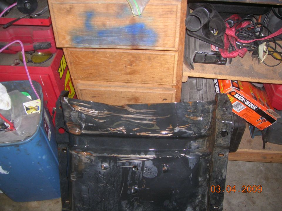 Damaged black metal vehicle part in front of wooden drawers and shelves with tools.