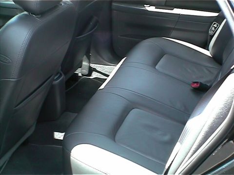2002 Ford Taurus - Interior shot of a sedan's rear bench seat in dark grey leather, taken through the open rear door of a four-door. The front seatback with a…