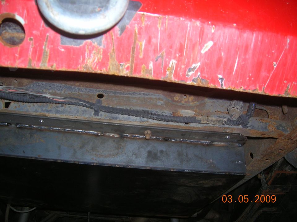 Underside of a red vehicle showing a welded frame crossmember