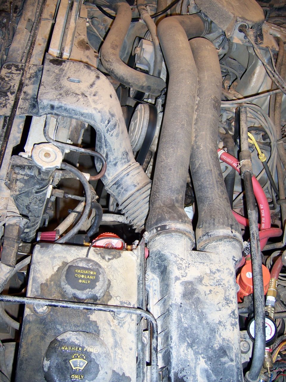 Photo of a dusty engine bay showing coolant reservoir and hoses