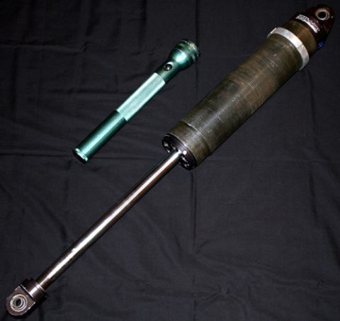 1984 Ford Bronco - A green flashlight rests on a black cloth next to a large, dark-colored shock absorber with a silver shaft. The shock absorber appears to b…