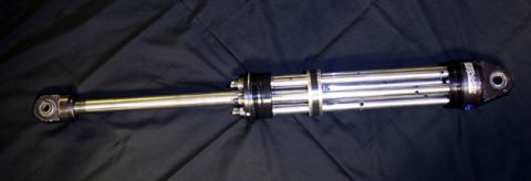 1984 Ford Bronco - A silver and black adjustable shock absorber is laid out horizontally on a black fabric background. The shock absorber has a threaded rod o…