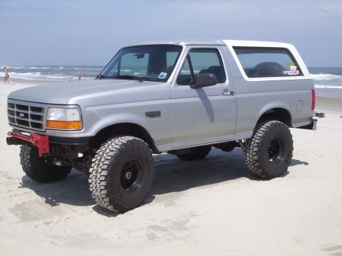 1995 Ford Bronco - Lifted 1995 Ford Bronco on a beach, showing its off-road tires and modified front bumper.